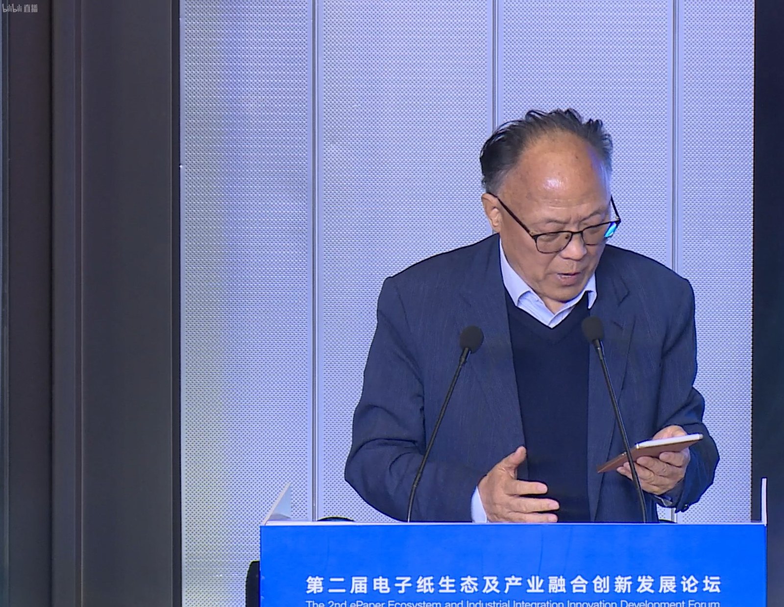 漢王科技董事長劉迎建在論壇講台後，手持一台小尺寸電子紙裝置唸講稿