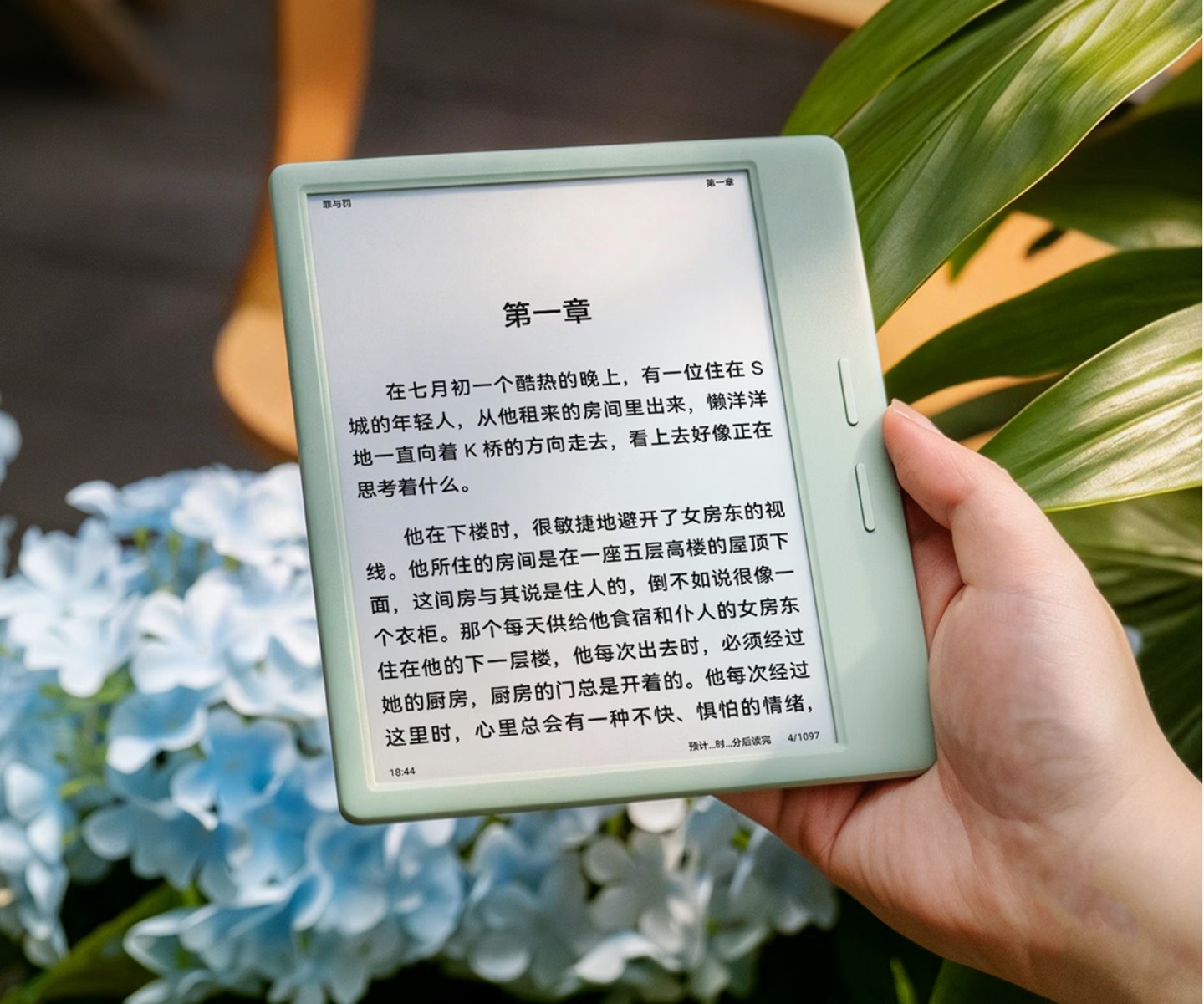 一手拿著淺綠色的掌閱 Ocean 6 Pro，螢幕顯示中文小說第一章，背景是藍色繡球花與綠色植物