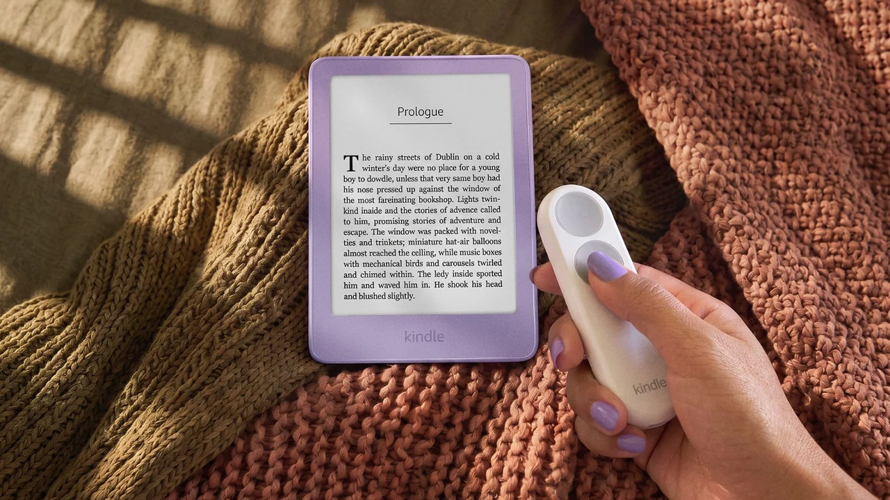 Amazon 官方情境圖:一隻手拿著白色的 Kindle Click 翻頁器,旁邊是放在針織毯上的淡紫色 Kindle,螢幕顯示小說的 Prologue 頁面