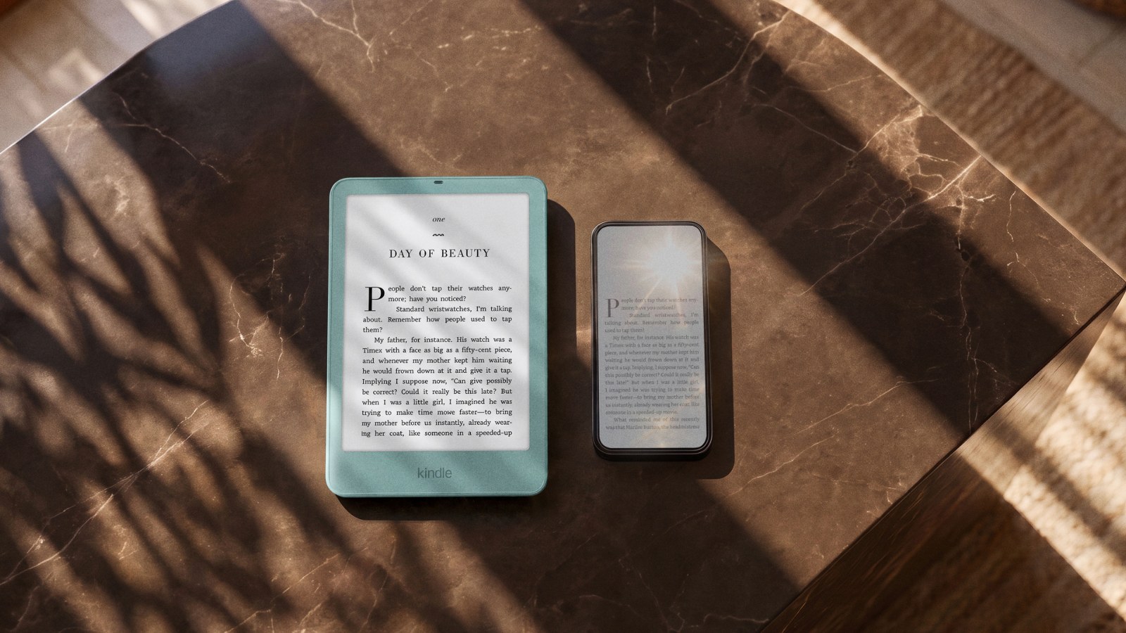 Amazon 官方情境圖:大理石桌面上,一台海玻璃綠色的新款 Kindle 放在手機旁邊,兩者都顯示書頁,Kindle 螢幕在陽光下沒有反光