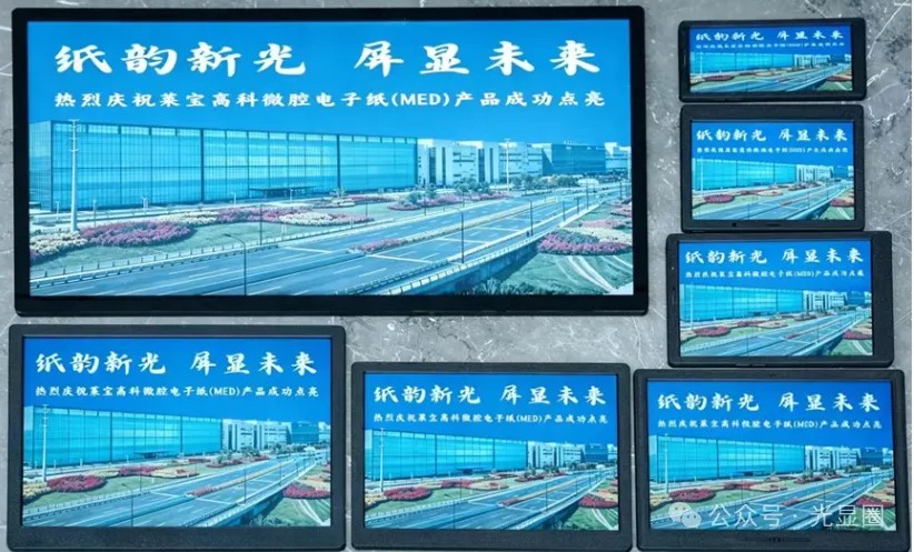 七片點亮的萊寶 MED 彩色電子紙並排放在大理石檯面上,一大六小,畫面都是藍天下的廠房與道路,上方寫著「紙韻新光 屏顯未來」與「熱烈慶祝萊寶高科微腔電子紙(MED)產品成功點亮」